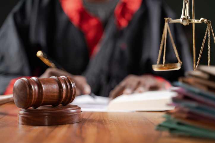 Focus on judge gavel, Unrecognizable judge busy writing verdict or making notes from the book with gavel and balance scale on table. iStock