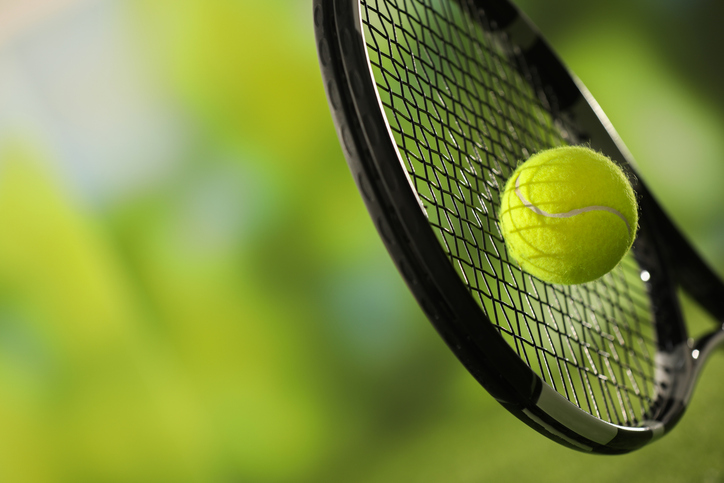 Tennis racket with ball against blurred green background, closeup. Space for text iStock